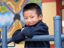 A smiling young boy in school uniform leaning on playground equipment